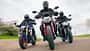 Ducatti Monster, BMW F900 R, Yamaha MT-09, Ducati Monster, Naked Bike, Motorradvergleich, Kurvenfahrt, Landstraße, Gruppenfahrt, Motorradtest Das Foto zeigt drei Naked Bikes in enger Kurvenfahrt: Ducatti Monster, BMW F900 R und Yamaha MT-09. Die Fahrer in vollständiger Schutzkleidung bewegen die Motorräder mit deutlicher Schräglage auf einer kurvigen Landstraße, Front- und Fahrwerksdetails sind klar erkennbar. Die Szene wirkt wie eine Gruppen- bzw. Vergleichsfahrt unter trockenen Bedingungen.