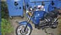BMW-Motorrad, Straßenmotorrad, Motorrad, Papiercontainer, Stadtumgebung, Altpapier, Zweirad, Parken, BMW Blaues BMW-Motorrad vor blauen Müllcontainern im Freien, teilweise von Pflanzen umgeben.
