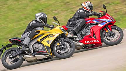 Das Foto zeigt eine Honda CBR 650R und eine Triumph Daytona 660 in sportlicher Schräglage auf einer Landstraßenkurve. Die beiden vollverkleideten Sportmotorräder werden von komplett ausgerüsteten Fahrern bewegt; am roten Bike ist der große HONDA‑Schriftzug sichtbar, die Triumph fährt in Gelb daneben. Laut IPTC handelt es sich bei der Honda um die CBR 650R mit E‑Clutch.
