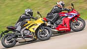 Das Foto zeigt eine Honda CBR 650R und eine Triumph Daytona 660 in sportlicher Schräglage auf einer Landstraßenkurve. Die beiden vollverkleideten Sportmotorräder werden von komplett ausgerüsteten Fahrern bewegt; am roten Bike ist der große HONDA‑Schriftzug sichtbar, die Triumph fährt in Gelb daneben. Laut IPTC handelt es sich bei der Honda um die CBR 650R mit E‑Clutch.
