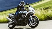 Yamaha Fazer 600 fährt in Kurvenfahrt auf Landstraße. Hintergrund eine ländliche Umgebung mit grünen Wiesen und ein dunkel bewölkter Himmel.