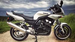 Silberne Yamaha Fazer 600, seitlich fotografiert, auf Feldweg mit bewölktem Himmel.