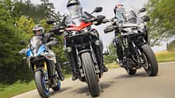 Drei Motorräder – Suzuki GSX-S1000 GX, Honda CB 1000 GT und Kawasaki Versys 1100 SE – fahren nebeneinander auf einer Landstraße. Die Aufnahme zeigt die Motorräder frontal in Bewegung mit Fahrern in voller Schutzkleidung. Die Umgebung ist grün und leicht verschwommen, was die Dynamik der Fahrt unterstreicht.