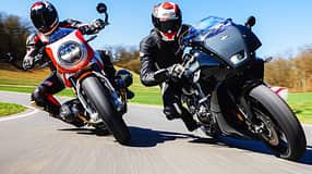 Eine BMW R 12 S und eine Yamaha XSR 900 GP werden auf einer Landstraße in Schräglage gefahren. Beide Fahrer tragen Motorradbekleidung und Helme. Die Szene zeigt eine dynamische Kurvenfahrt bei sonnigem Wetter.
