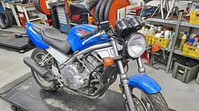 Honda CB-1 in blauer Lackierung auf einer Werkstattbühne, umgeben von Werkstattregalen und Werkzeugen.