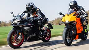 Zwei Sportmotorräder, QJ Motor SRK 921 RR und KTM 990 RC R, werden auf einer Landstraße gefahren. Beide Fahrer tragen Motorradbekleidung und Integralhelme. Die Aufnahme zeigt die Motorräder in voller Fahrt bei Tageslicht.