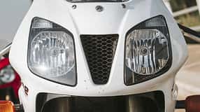 Die Detailaufnahme zeigt die Frontverkleidung eines Honda‑Sportmotorrads mit deutlich sichtbarem Honda‑Schriftzug. Zu sehen sind zwei große Doppelscheinwerfer und ein zentraler, dreieckiger Lufteinlass mit Wabengitter; unten sind die Standrohre der Telegabel sowie die Blinker erkennbar.