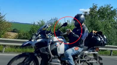 Motorradfahrer auf der Autobahn, mit beiden Händen am Smartphone