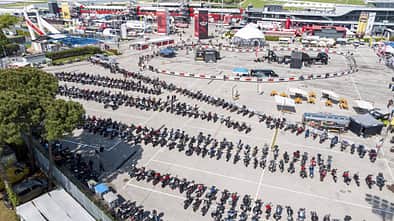Luftaufnahme eines großen Motorrad-Events mit zahlreichen Motorrädern auf einem Parkplatz und Event-Areal mit Messeständen.