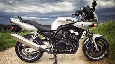 Silberne Yamaha Fazer 600, seitlich fotografiert, auf Feldweg mit bewölktem Himmel.