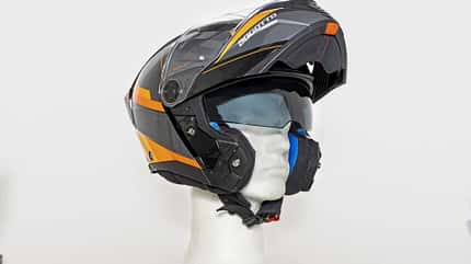 Der Bogotto FF404 Ezion Klapphelm ist auf einem neutralen Hintergrund abgebildet. Der Motorradhelm ist in Schwarz mit orangefarbenen Akzenten gestaltet und befindet sich in geöffneter Position auf einem weißen Styroporkopf. Das Visier und das integrierte Sonnenvisier sind sichtbar.