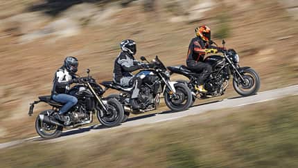 Drei Motorräder im direkten Vergleich: QJMOTOR SRK 600 PRO, Suzuki SV 650 und Yamaha MT 07 (alt) fahren nebeneinander auf einer Landstraße. Die Fahrer tragen Motorradschutzkleidung und Helme. Die Szene zeigt eine dynamische Fahrsituation im Freien.