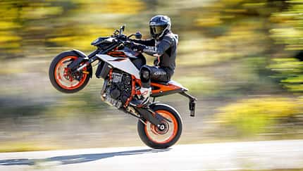 KTM 990 Duke R, Naked Bike, Wheelie, Motorrad, Straßenmotorrad, Zweizylinder, 2026, KTM, Stunt, Fahrdynamik KTM 990 Duke R, Naked Bike, wird auf dem Hinterrad gefahren (Wheelie), Fahrer in Motorradkombi, dynamische Straßenaufnahme.
