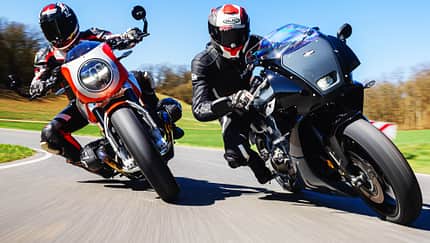 Eine BMW R 12 S und eine Yamaha XSR 900 GP werden auf einer Landstraße in Schräglage gefahren. Beide Fahrer tragen Motorradbekleidung und Helme. Die Szene zeigt eine dynamische Kurvenfahrt bei sonnigem Wetter.