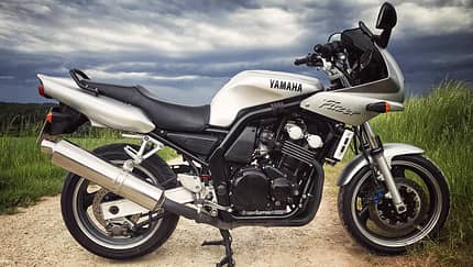 Yamaha Fazer 600, Vierzylinder, Tourenmotorrad, Landstraße, Feldweg Silberne Yamaha Fazer 600, seitlich fotografiert, auf Feldweg mit bewölktem Himmel.