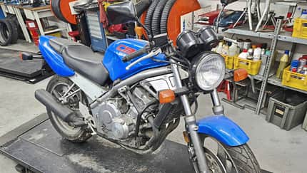 Honda CB-1 in blauer Lackierung auf einer Werkstattbühne, umgeben von Werkstattregalen und Werkzeugen.
