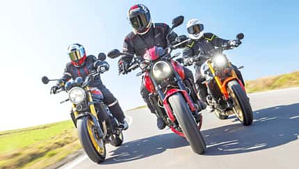 Kawasaki Z900RS SE, Triumph Trident 800, Yamaha XSR900, Naked Bike, Vergleichstest, Landstraße, MRD Heft 10/26, Motorrad, Dreiervergleich, Fahrdynamik Drei Naked Bikes (Kawasaki Z900RS SE, Triumph Trident 800, Yamaha XSR900) fahren nebeneinander auf einer Landstraße, aufgenommen aus der Froschperspektive. Die Fahrer tragen Motorradbekleidung und Integralhelme, im Hintergrund ist ein Windrad zu sehen.
