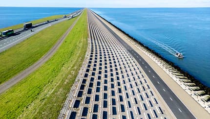 Damm, Autobahn, Luftaufnahme, Küstenstraße, Verkehrsinfrastruktur, Meer, Radweg, Holland, Wasserbau, Deich Luftaufnahme eines langen Damms mit Autobahn und Radweg, flankiert von Wasser auf beiden Seiten. Mehrere Fahrzeuge und ein Boot sind sichtbar.