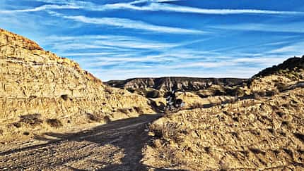 Reiseenduro steht auf einer staubigen Offroad-Piste in einer kargen, felsigen Wüstenlandschaft unter blauem Himmel.
