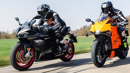QJ Motor SRK 921 RR, KTM 990 RC R, Supersportler, Sportmotorrad, Motorradvergleich, Landstraße, Zweizylinder, 2024, Motorradtechnik, Gruppenbild Zwei Sportmotorräder, QJ Motor SRK 921 RR und KTM 990 RC R, werden auf einer Landstraße gefahren. Beide Fahrer tragen Motorradbekleidung und Integralhelme. Die Aufnahme zeigt die Motorräder in voller Fahrt bei Tageslicht.