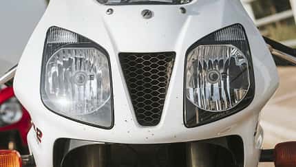 Honda-Supersportler, Sportmotorrad, Motorradfront, Frontverkleidung, Doppelscheinwerfer, Lufteinlass, Wabengitter, Telegabel, Blinker Die Detailaufnahme zeigt die Frontverkleidung eines Honda‑Sportmotorrads mit deutlich sichtbarem Honda‑Schriftzug. Zu sehen sind zwei große Doppelscheinwerfer und ein zentraler, dreieckiger Lufteinlass mit Wabengitter; unten sind die Standrohre der Telegabel sowie die Blinker erkennbar.