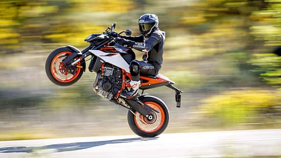 KTM 990 Duke R, Naked Bike, wird auf dem Hinterrad gefahren (Wheelie), Fahrer in Motorradkombi, dynamische Straßenaufnahme.
