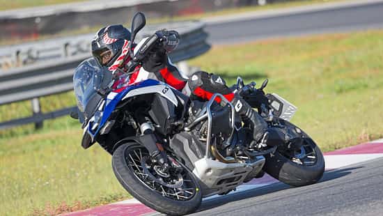 Reiseenduro-Motorrad in Kurvenfahrt auf Rennstrecke, Fahrer mit Schutzkleidung und Helm.