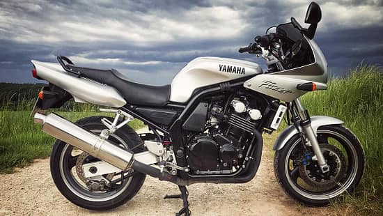 Silberne Yamaha Fazer 600, seitlich fotografiert, auf Feldweg mit bewölktem Himmel.