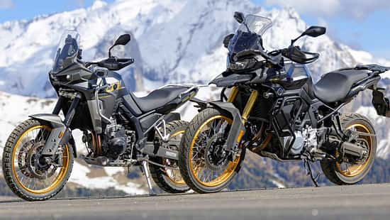 Zwei Mid-Adventure-Motorräder asiatischer Hersteller vor schneebedeckten Alpenbergen, aufgenommen beim Alpenmaster-Event 2026.