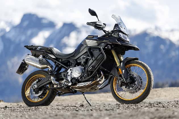 Moto Voge DS 900 X Adventure avec jantes à rayons dorées sur fond de montagne alpine, vue de côté