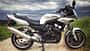 Yamaha Fazer 600, Vierzylinder, Tourenmotorrad, Landstraße, Feldweg Silberne Yamaha Fazer 600, seitlich fotografiert, auf Feldweg mit bewölktem Himmel.