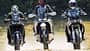 CFMOTO 1000MT-X, Ducati DesertX, Honda CRF1100L Africa Twin, Reiseenduro, Adventure-Bike, Vergleichstest, Offroad-Fahrt, Schotterstraße, Dreiervergleich, Motorrad Die Aufnahme zeigt drei Reiseenduros in der Frontansicht: CFMOTO 1000MT-X, Ducati DesertX und Honda CRF1100L Africa Twin. Die Adventure-Bikes fahren nebeneinander auf einer Schotterstraße, mit hohen Windschilden und Handprotektoren gut erkennbar. Im leichten Offroad-Einsatz wirbeln sie Staub auf, die Szene wirkt wie ein Vergleichslauf im Gelände.