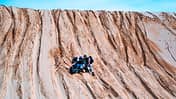 Fahrer hebt an einem steilen Hang aus Sand sein Motorrad auf