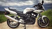 Silberne Yamaha Fazer 600, seitlich fotografiert, auf Feldweg mit bewölktem Himmel.