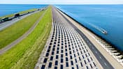 Damm, Autobahn, Luftaufnahme, Küstenstraße, Verkehrsinfrastruktur, Meer, Radweg, Holland, Wasserbau, Deich Luftaufnahme eines langen Damms mit Autobahn und Radweg, flankiert von Wasser auf beiden Seiten. Mehrere Fahrzeuge und ein Boot sind sichtbar.