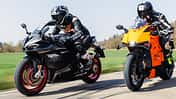 Zwei Sportmotorräder, QJ Motor SRK 921 RR und KTM 990 RC R, werden auf einer Landstraße gefahren. Beide Fahrer tragen Motorradbekleidung und Integralhelme. Die Aufnahme zeigt die Motorräder in voller Fahrt bei Tageslicht.